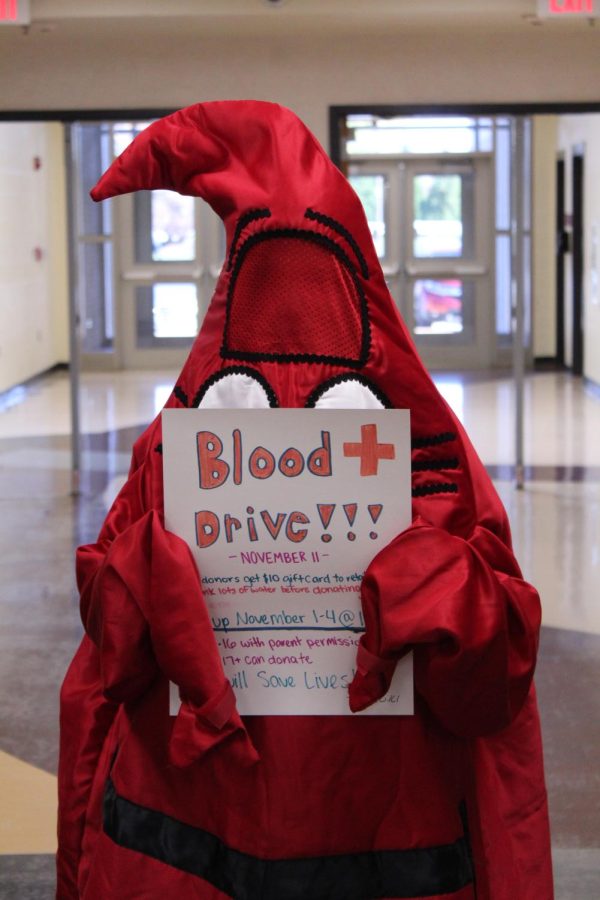 A drop of blood costume holds a blood drive sign.